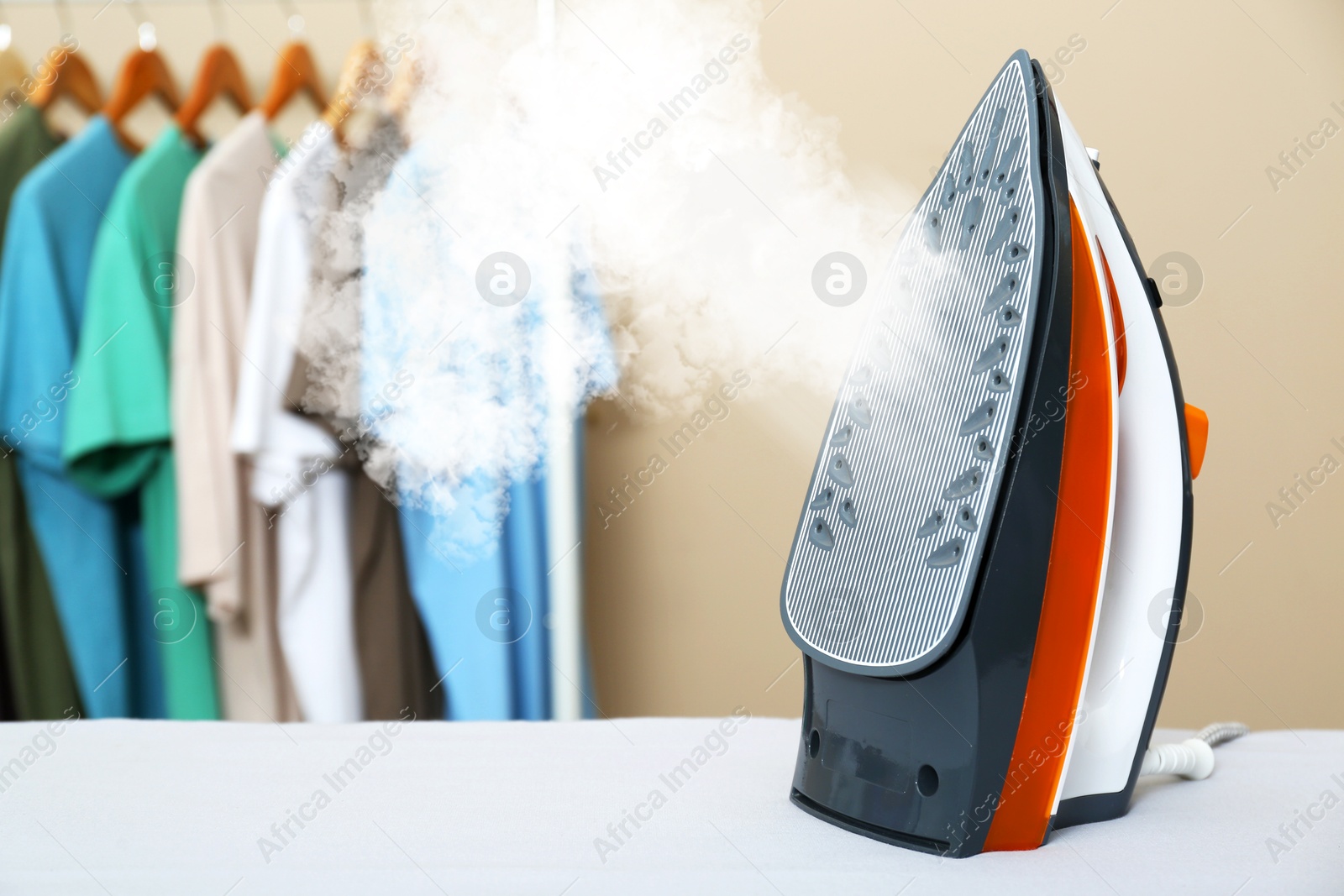 Image of Steam coming out of clothes iron against clothing rack indoors