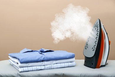 Image of Steam coming out of clothes iron and folded garment against dark beige background