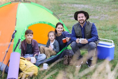 Photo of Happy family spending time together with camping tent, tourist equipment and mugs of hot drink outdoors
