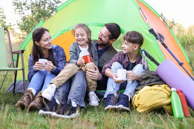 Photo of Happy family spending time together with camping tent, tourist equipment and mugs of hot drink outdoors