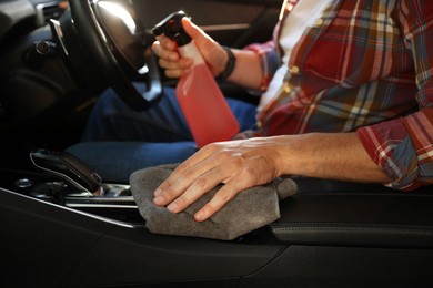 Photo of Man wiping car center console with grey microfiber rag in salon, closeup