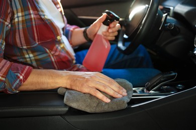 Photo of Man wiping car center console with grey microfiber rag in salon, closeup