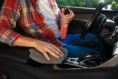 Photo of Man wiping car center console with grey microfiber rag in salon, closeup