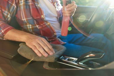 Photo of Man wiping car center console with grey microfiber rag in salon, closeup