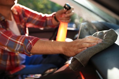 Photo of Man wiping car dashboard with grey microfiber rag in salon, closeup