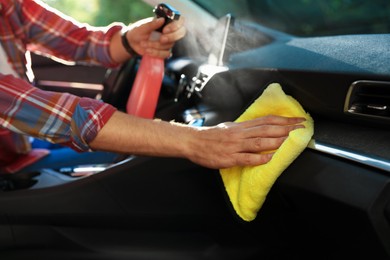 Photo of Man wiping car dashboard with yellow microfiber rag in salon, closeup