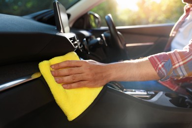 Photo of Man wiping car dashboard with yellow microfiber rag in salon, closeup
