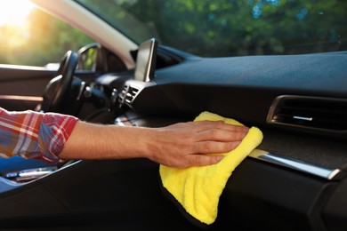 Photo of Man wiping car dashboard with yellow microfiber rag in salon, closeup