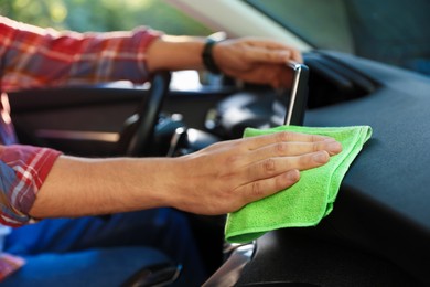 Photo of Man wiping car dashboard with green microfiber rag in salon, closeup