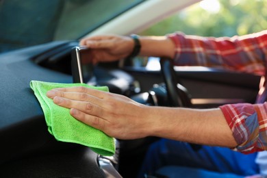 Photo of Man wiping car dashboard with green microfiber rag in salon, closeup