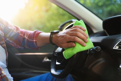 Photo of Man wiping steering wheel with green microfiber rag in car salon, closeup