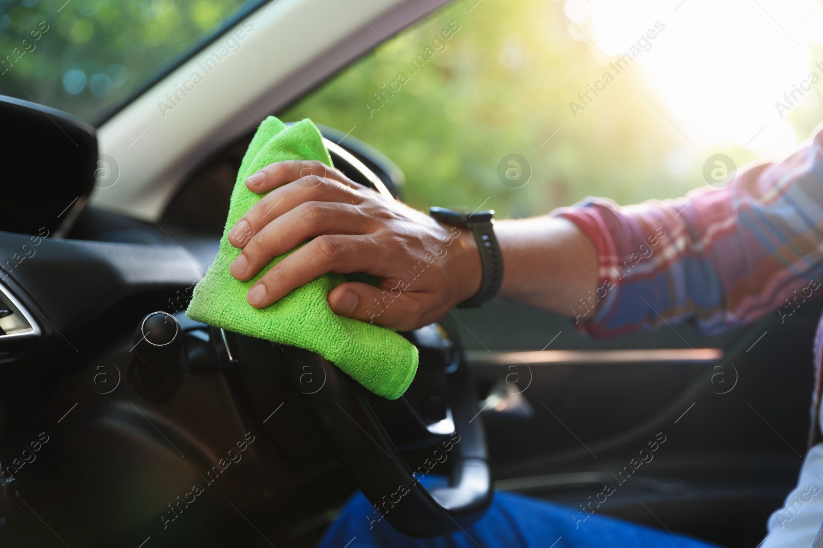 Photo of Man wiping steering wheel with green microfiber rag in car salon, closeup