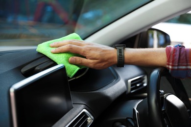 Photo of Man wiping car dashboard with green microfiber rag in salon, closeup