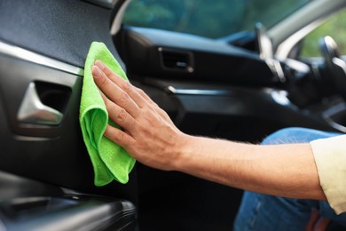 Photo of Man wiping car door with green microfiber rag in salon, closeup