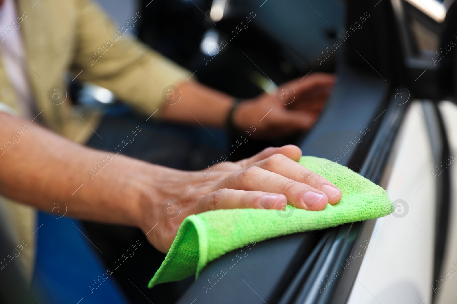 Photo of Man wiping car door with green microfiber rag in salon, closeup