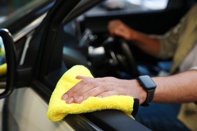 Photo of Man wiping car door with yellow microfiber rag in salon, closeup