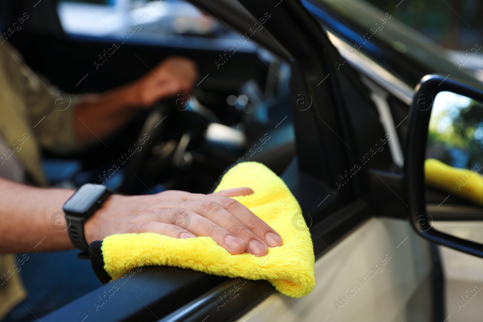 Photo of Man wiping car door with yellow microfiber rag in salon, closeup