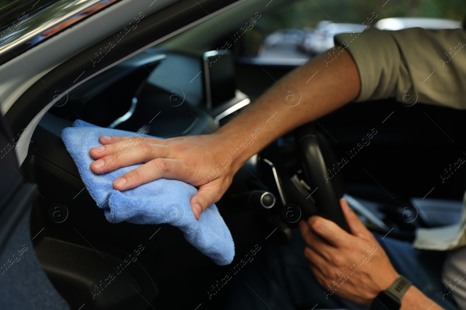 Photo of Man wiping car interior with blue microfiber rag in salon, closeup
