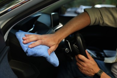 Photo of Man wiping car interior with blue microfiber rag in salon, closeup