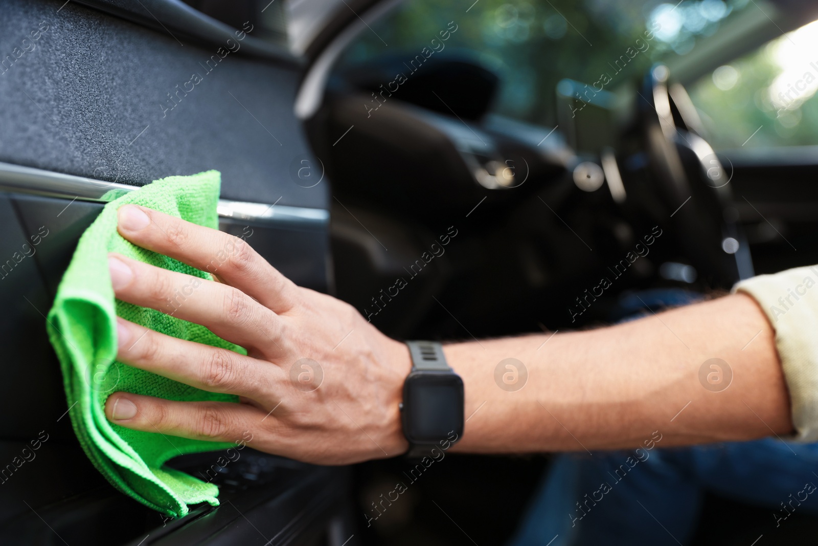 Photo of Man wiping car door with green microfiber rag in salon, closeup