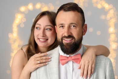 Photo of Making marriage proposal. Woman with engagement ring and her happy fiance hugging on light grey background with blurred lights, bokeh effect