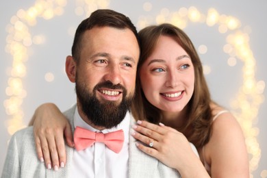 Photo of Making marriage proposal. Woman with engagement ring and her happy fiance hugging on light grey background with blurred lights, bokeh effect