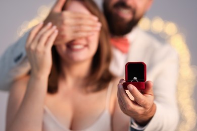 Photo of Man with engagement ring making marriage proposal to his girlfriend on light grey background with blurred lights, selective focus. Bokeh effect