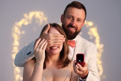 Photo of Man with engagement ring making marriage proposal to his girlfriend on light grey background with blurred lights, bokeh effect