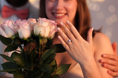Photo of Making marriage proposal. Woman with engagement ring and her happy fiance on light grey background, selective focus. Bokeh effect