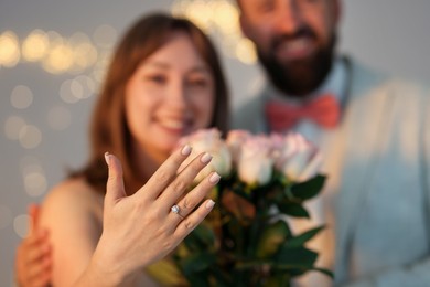 Photo of Making marriage proposal. Woman with engagement ring and her happy fiance on light grey background, selective focus. Bokeh effect