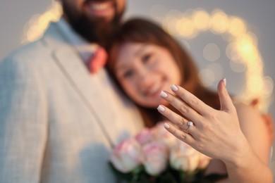Photo of Making marriage proposal. Woman with engagement ring and her fiance on light grey background, selective focus. Bokeh effect