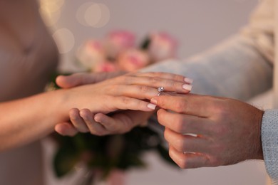 Photo of Making marriage proposal. Man putting engagement ring on his girlfriend's finger against blurred background, closeup. Bokeh effect