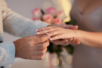 Photo of Making marriage proposal. Man putting engagement ring on his girlfriend's finger against blurred background, closeup. Bokeh effect