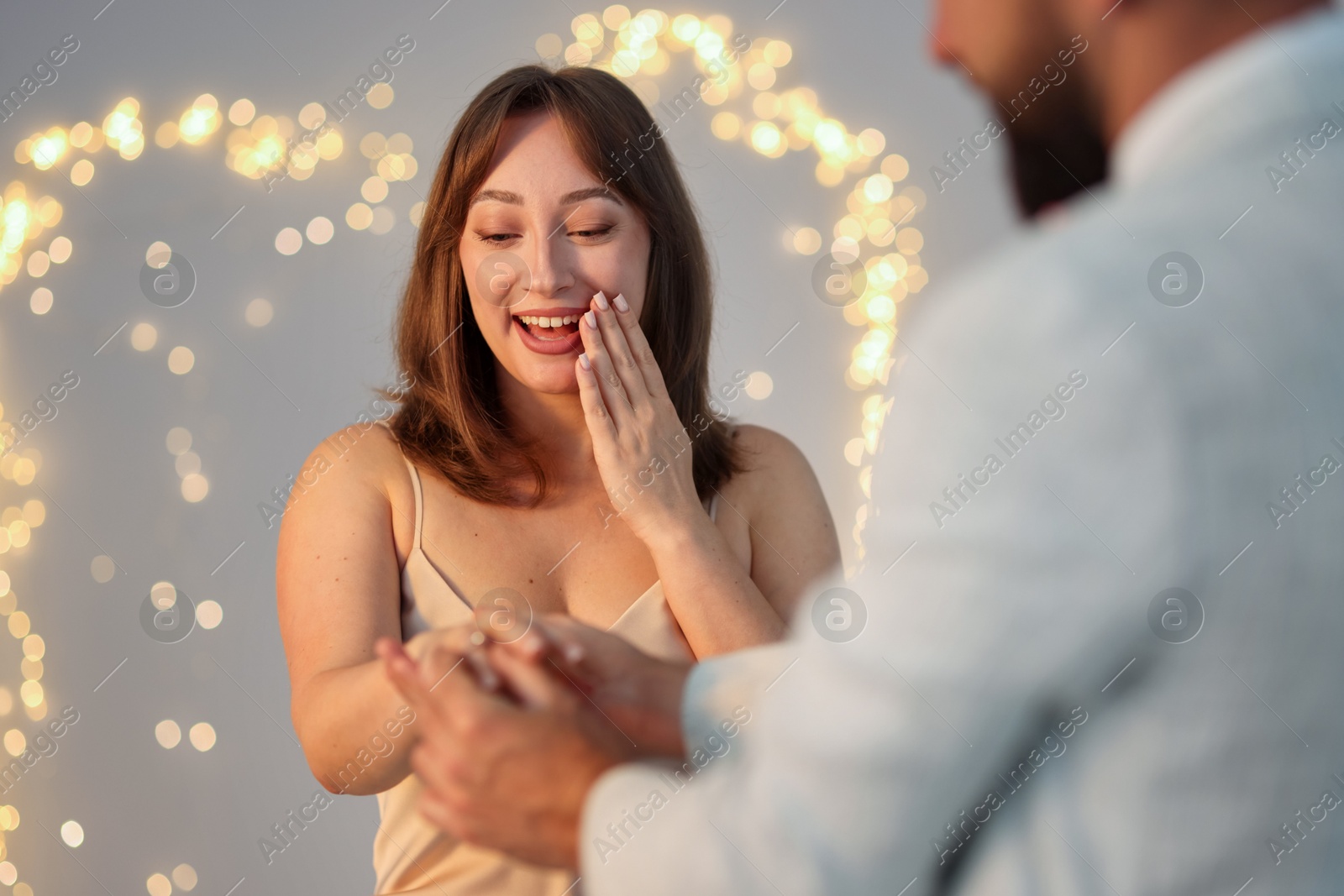 Making marriage proposal. Man putting engagement ring on his girlfriend's finger against light grey background, closeup. Bokeh effect Photo of Making marriage proposal. Man putting engagement ring on his girlfriend's finger against light grey background, closeup. Bokeh effect
