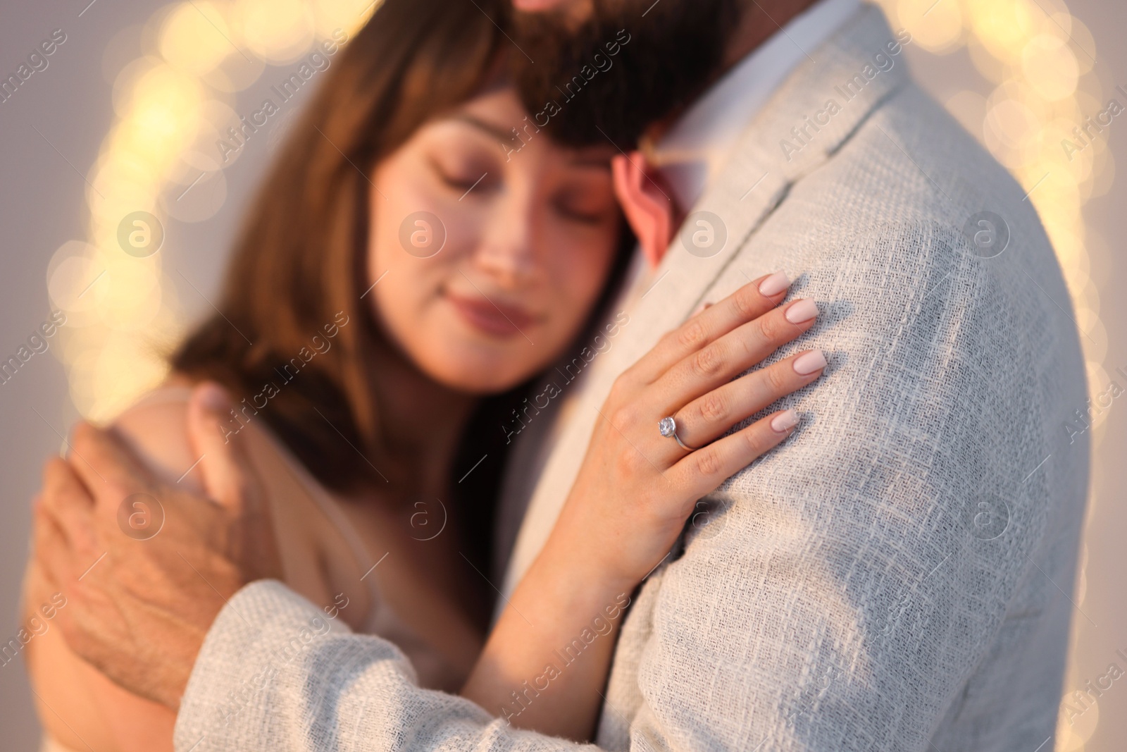 Making marriage proposal. Woman with engagement ring and her fiance hugging on light grey background, bokeh effect Photo of Making marriage proposal. Woman with engagement ring and her fiance hugging on light grey background, bokeh effect