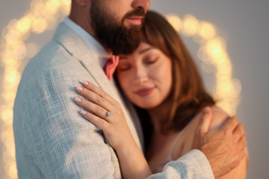 Photo of Making marriage proposal. Woman with engagement ring and her fiance hugging on light grey background, bokeh effect