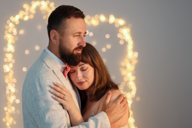 Photo of Making marriage proposal. Woman with engagement ring and her fiance hugging on light grey background, space for text. Bokeh effect