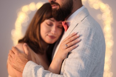 Photo of Making marriage proposal. Woman with engagement ring and her fiance hugging on light grey background, bokeh effect