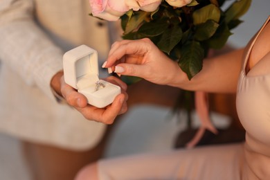 Photo of Man with engagement ring and bouquet of flowers making marriage proposal to his girlfriend on blurred background, closeup