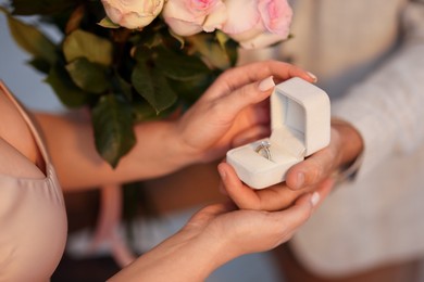 Photo of Man with engagement ring and bouquet of flowers making marriage proposal to his girlfriend on blurred background, closeup