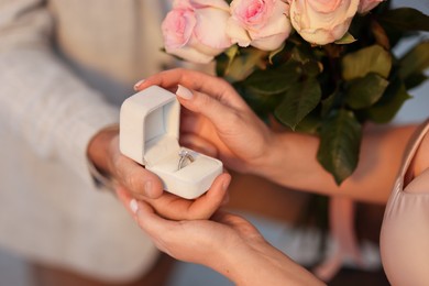 Photo of Man with engagement ring and bouquet of flowers making marriage proposal to his girlfriend on blurred background, closeup