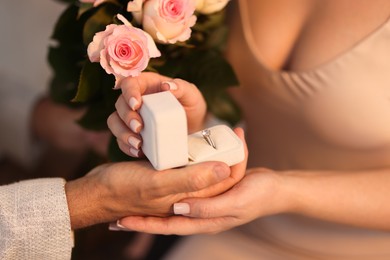 Photo of Man with engagement ring and bouquet of flowers making marriage proposal to his girlfriend on blurred background, closeup