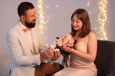 Photo of Man with engagement ring making marriage proposal to his girlfriend on light grey background with blurred lights, bokeh effect