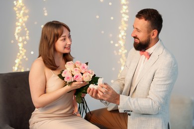 Photo of Man with engagement ring making marriage proposal to his girlfriend on light grey background with blurred lights, bokeh effect