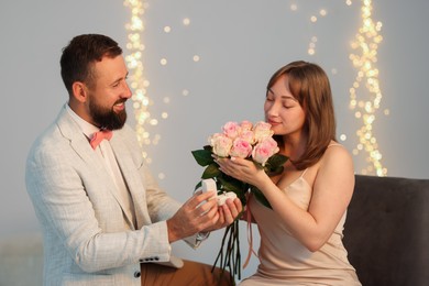 Photo of Man with engagement ring making marriage proposal to his girlfriend on light grey background with blurred lights, bokeh effect