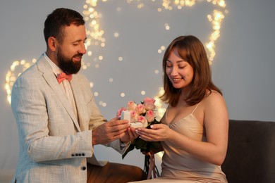 Photo of Man with engagement ring making marriage proposal to his girlfriend on light grey background with blurred lights, bokeh effect