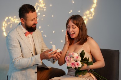 Photo of Man with engagement ring making marriage proposal to his girlfriend on light grey background with blurred lights, bokeh effect