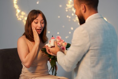 Photo of Man with engagement ring making marriage proposal to his girlfriend on light grey background with blurred lights, bokeh effect