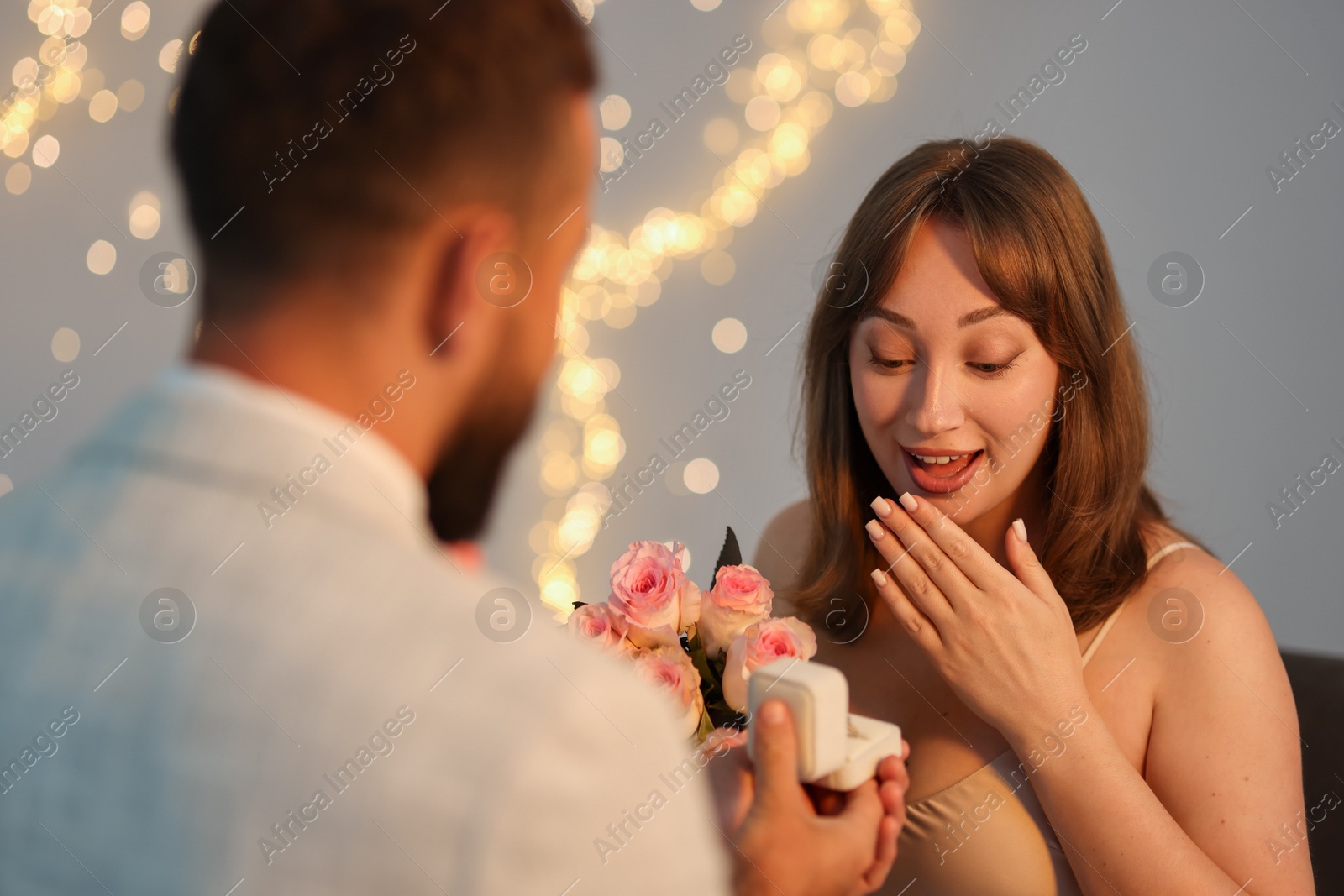 Photo of Man with engagement ring making marriage proposal to his girlfriend on light grey background with blurred lights, bokeh effect