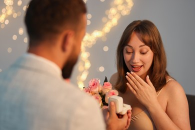Photo of Man with engagement ring making marriage proposal to his girlfriend on light grey background with blurred lights, bokeh effect